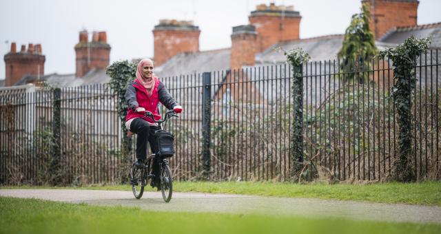 Woman smiles as she pedals electric Brompton through park.