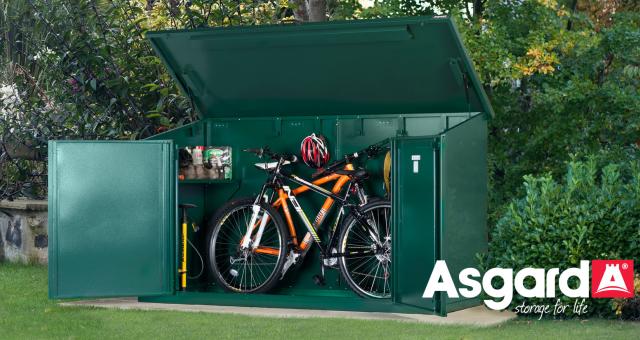 Two mountain bikes and a floor pump are in a green Asgard bike storage shed in a garden. The Asgard logo is on the bottom right of the photo