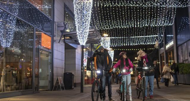 3 people walking with their bikes past Christmas lights © Joolze Dymond