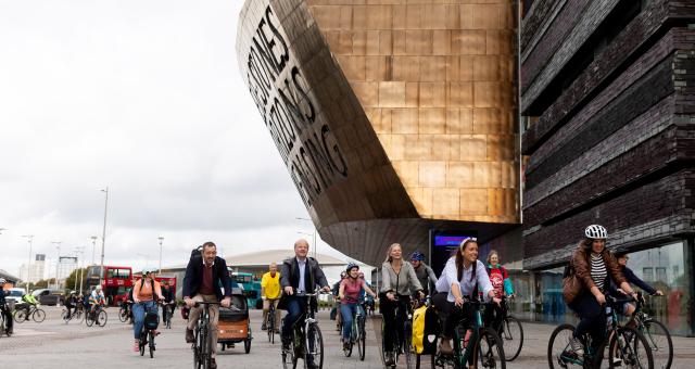 A large group of people are cycling round the Senedd building in Cardiff