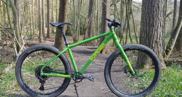 A rigid mountain bike stands in the middle of a woodland trail