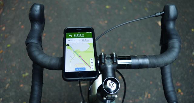 Point of view of a bicycle's handlebars, a phone is mounted to the left hand side, a map showing the route to follow