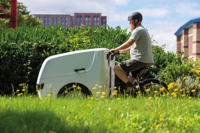 A man is cycling an e-cargo bike through a grassy field