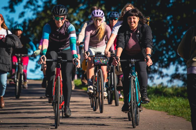 Group of women all cycling together on a path towards the camera