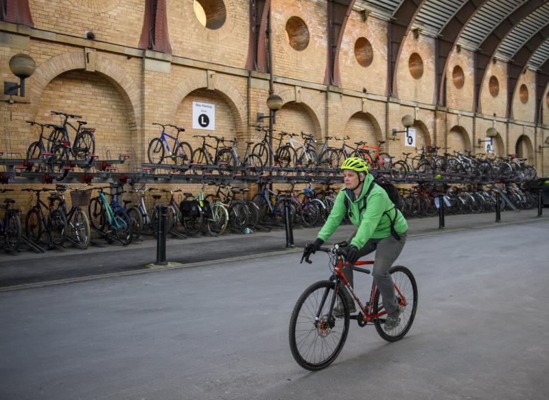 A cyclist riding past a large bike parking area in a train station.