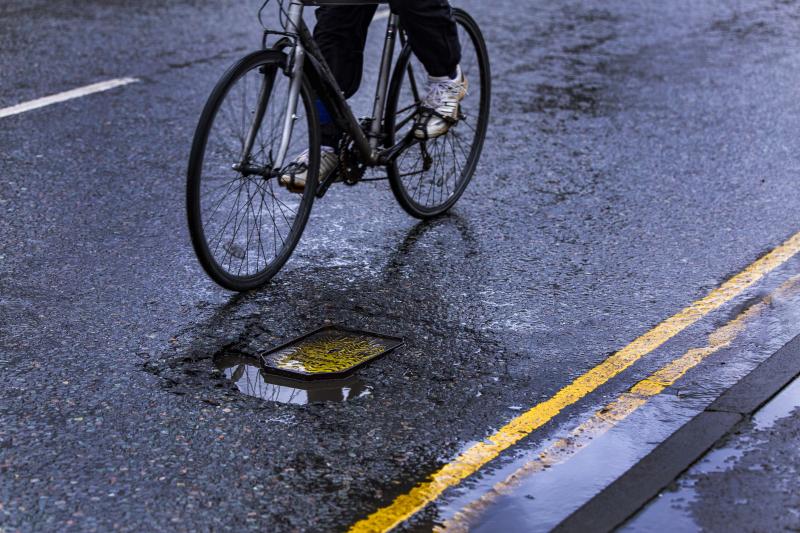 A person on a bicycle is riding around a pothole in the road