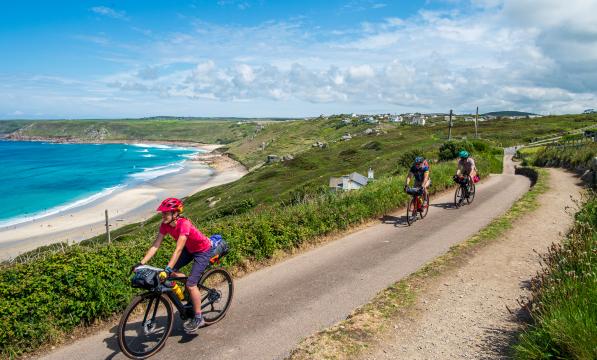 3 cyclists on the West Kernow Way route in Cornwall cycling on a path next to the sea