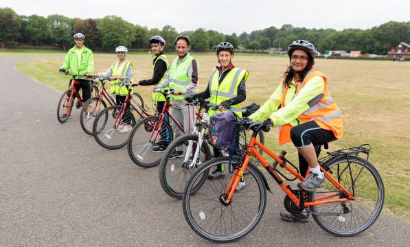 A group of people is on a tarmac path next to a field. They are all on bikes and look ready to set off on a ride