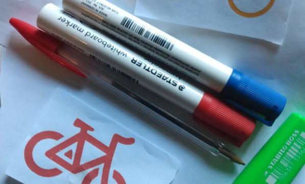 Two board markers, a red pen, a green pen and red and yellow line pictures of bicycles on a white backdrop