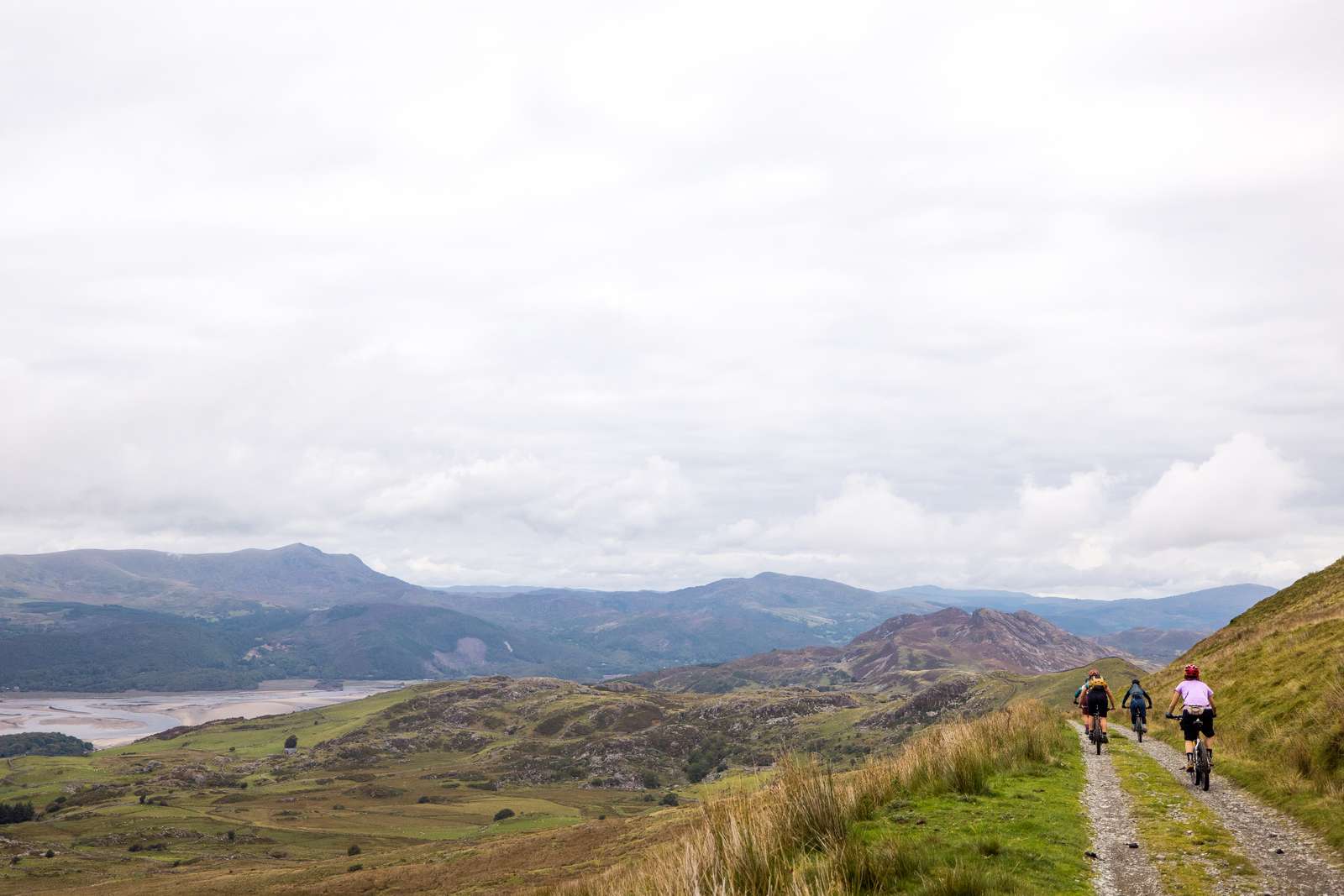 Three people cycle along a gravel track towards mountains
