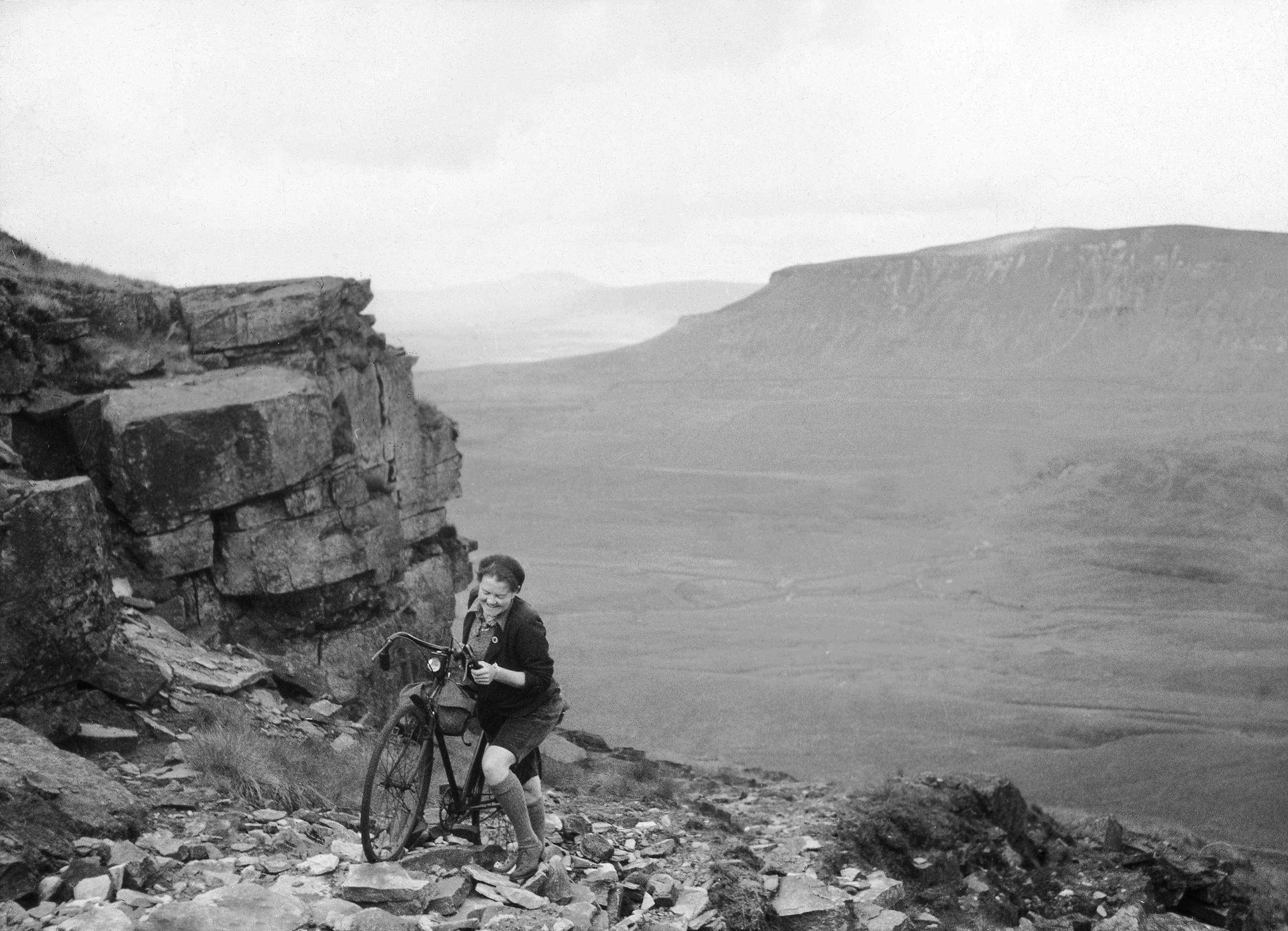 B+W photo of a woman pushes her bike up rough terrain