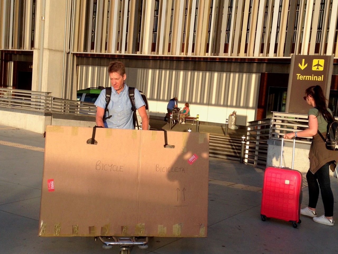 A man pushes a cardboard box labelled bike on an airport trolley