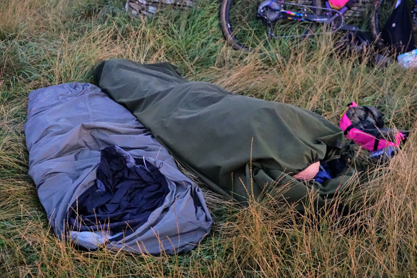 Two bivvy bags with one sleeper laid out in a field