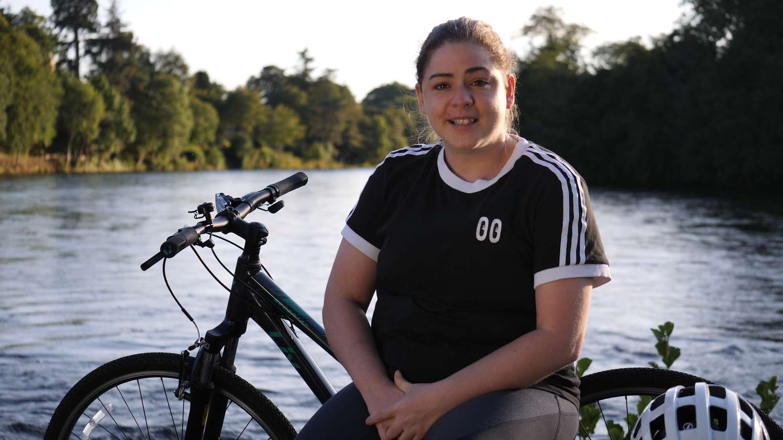 A young woman sat by a lake with her bicycle