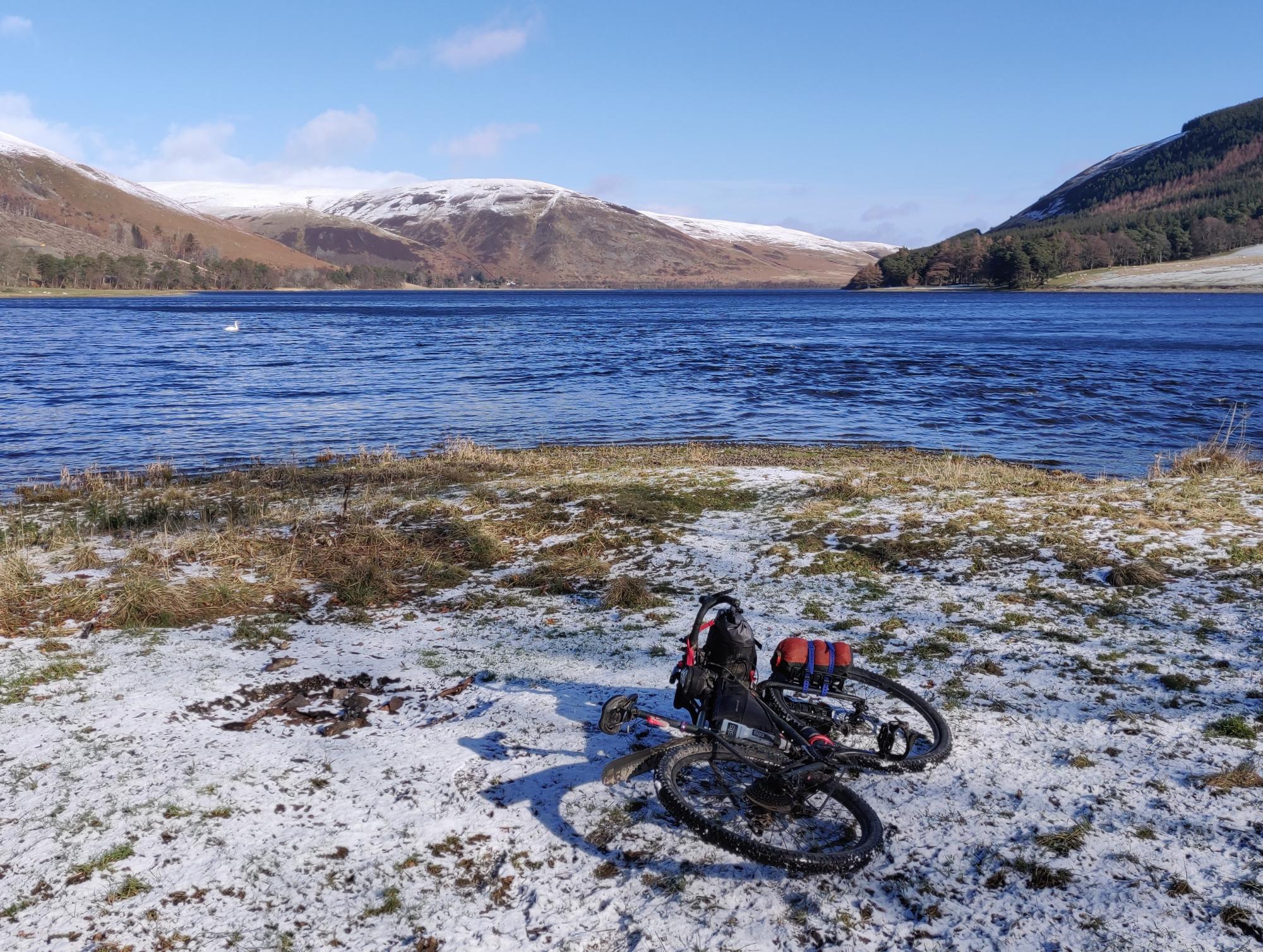 Bike resting in the snow in front of a loch