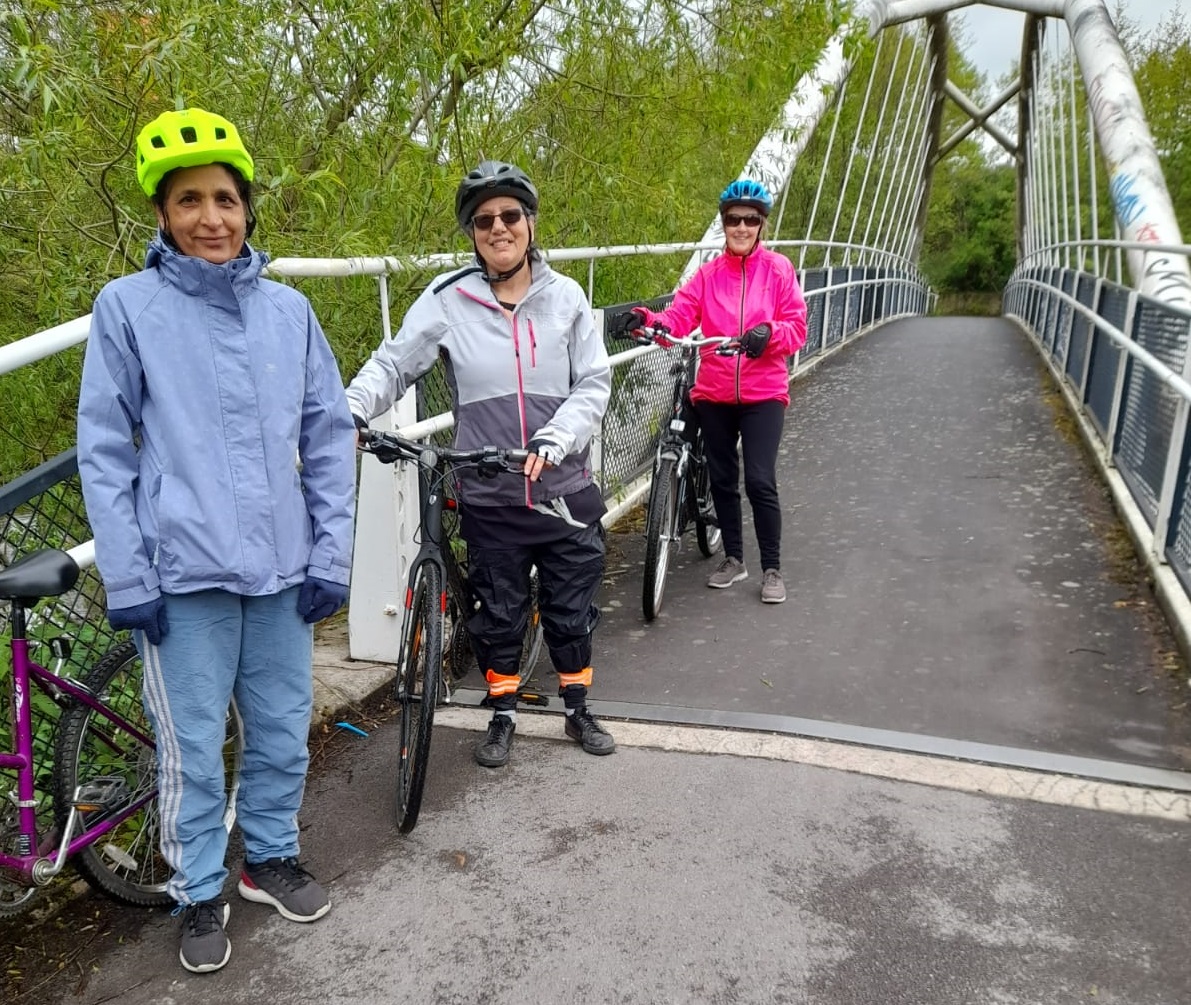 photo of 3 women standing with their bikes next to a bridge