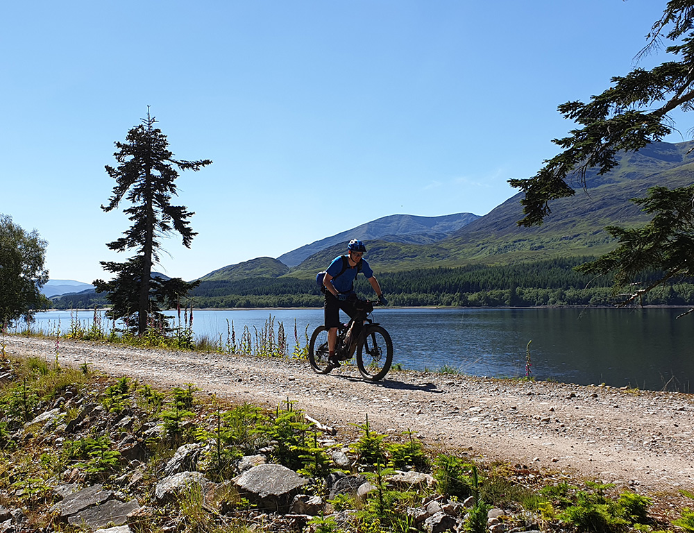 A cyclist riding a mountain bike along the shores of a Loch on a sunny day