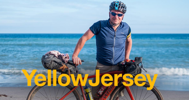Male presenting person on the beach with a 'Yellow Jersey' logo overlaying