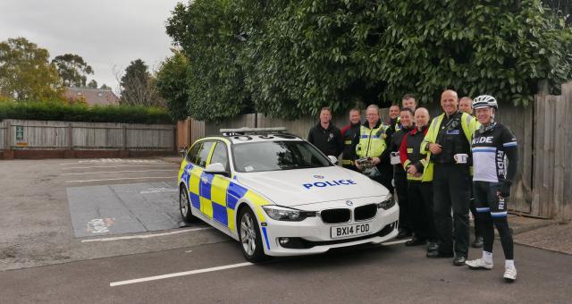 A group of police officers gathered around a marked police vehicle in a residential street