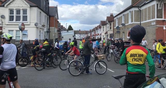 A large group of people are cycling on the road. There is a wide range of bikes and diversity of people