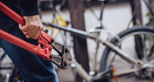 A person is carrying a heavy-duty bolt cutter towards a locked silver bike