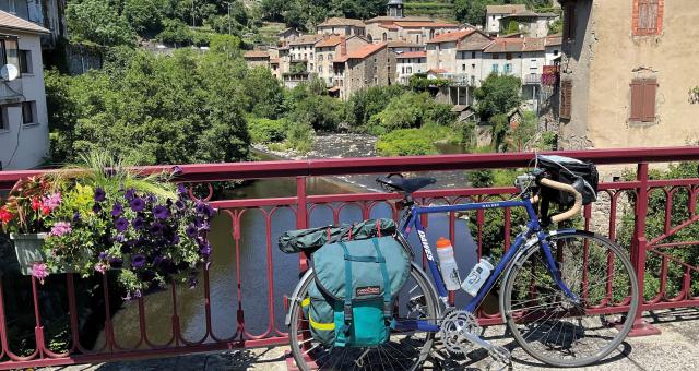 A blue touring bike is leaning against a red fence on a bridge over a stream in a town in France