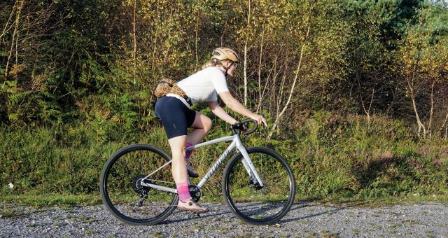 A woman is cycling on a grey Specialized gravel bike on an off-road gravel track