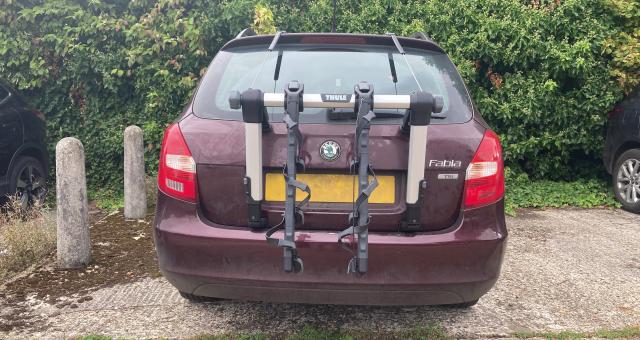 The Thule rack is fitted to the back of a purple Skoda Fabia that's parked in front of a hedge