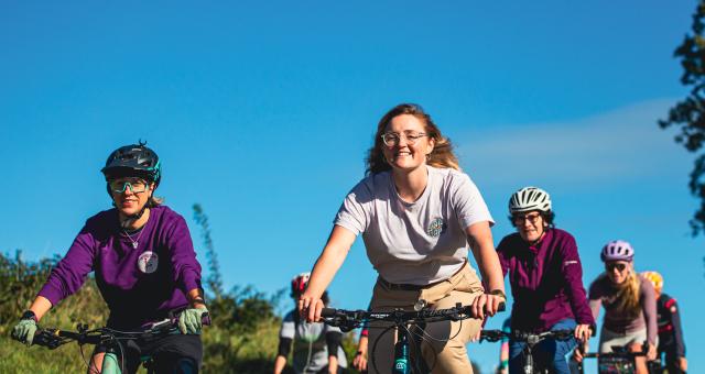 A group of women are cycling on a bright sunny day. Some are wearing helmets some are not.