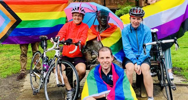 A group of people is posing with rainbow flags and their bikes