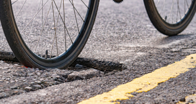 A bike wheel moving through a pothole in a road.