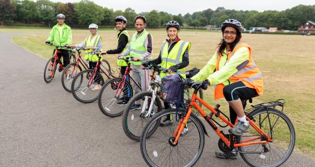 A group of people is on a tarmac path next to a field. They are all on bikes and look ready to set off on a ride