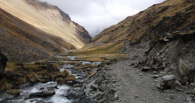 A mountain valley with rocky gravel track and a stream running alongside