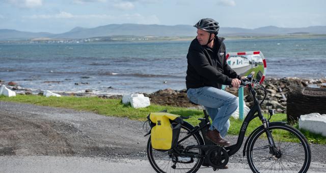 A cyclist on an ebike, carrying panniers along a coastal road.