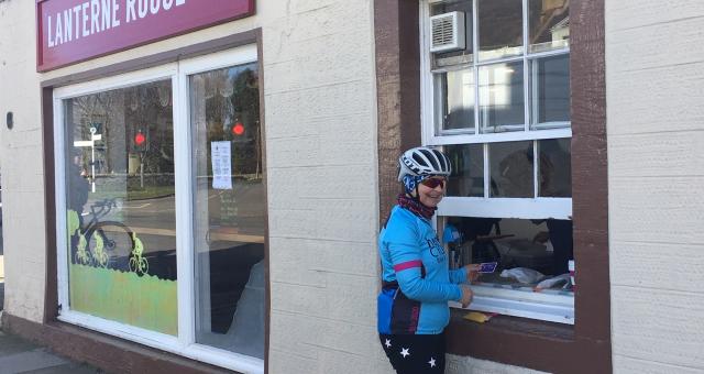A female cyclists collects a takeaway coffee from a serving hatch at a roadside cafe