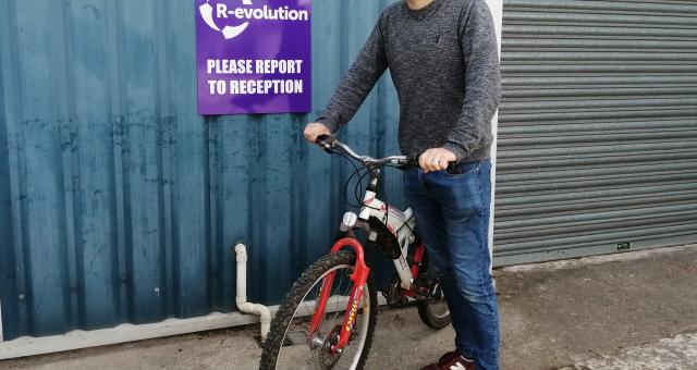 Man sands with his bicycle in front of a blue corrugated wall and a garage door