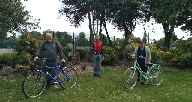 A man and a woman stand holding new bicycles while a man in a red tracksuit top stands between them