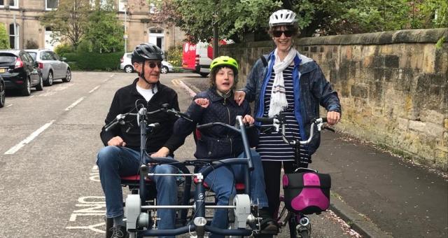 Father and daughter on side-by-side tandem with mother standing next to them on solo bike