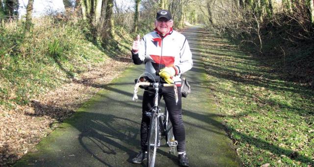 Man in white jacket with red stride gives a thumbs up while astride a bicycle