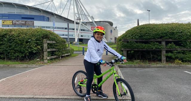 A young boy poses on a bicycle outside a large football stadium