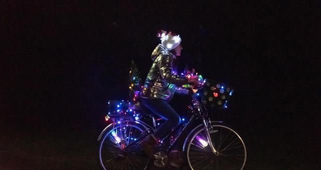 A woman riding a bike covered in Christmas lights.