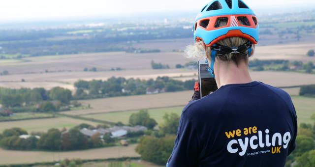 Female cyclist wearing Cycling UK t-shirt taking photo of stunning landscape on phone