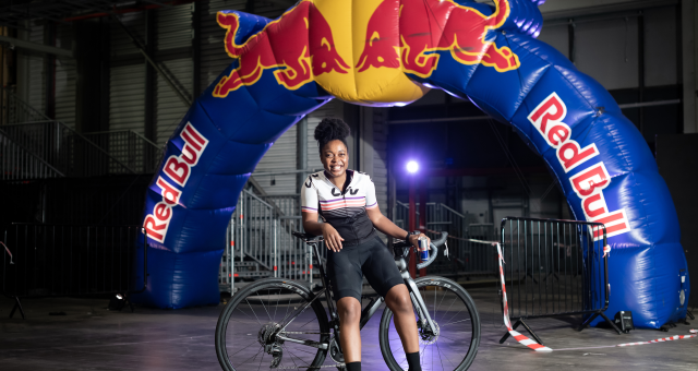 Woman leaning on a road bike while standing in front of a Red Bull branded arch