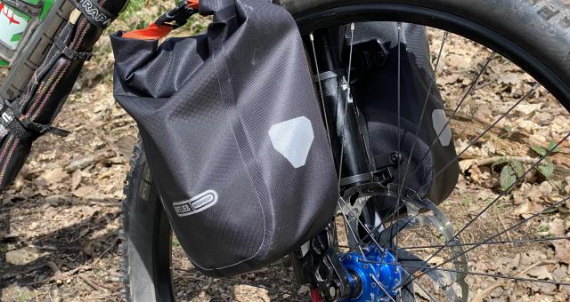 A close-up of a packed Ortlieb Fork Pack attached to a mountain bike front fork