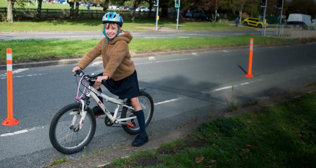 A young girl in a school uniform sits on her bike in a cycle lane