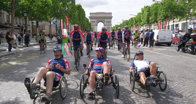 three men side by side on recumbent trikes with Arc de Triomphe in the background