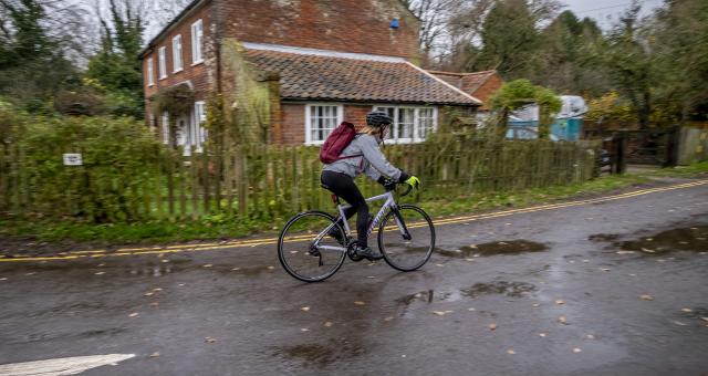 A woman cycles on a wet road with puddles and leaves scattered on it
