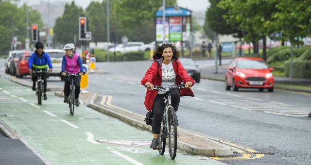 Three people pedal on green cycle lane next to busy road in the city