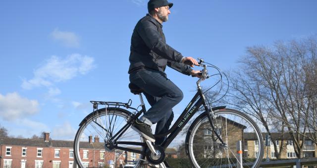 A man is riding a black step-through roadster along a suburban street