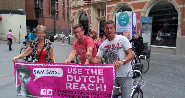 3 people hold banner, promoting the Dutch Reach to improve cycle safety